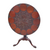 A round wooden table with intricate carvings around the edge, featuring a floral motif in the center, with a simple triangular pedestal base.
