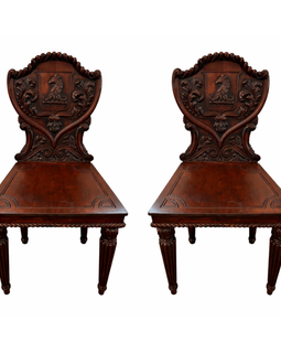 Pair of English William IV carved mahogany hall chairs, c.1830, with heraldic shield backs, horse‑head cresting, acanthus carving, solid seats, and fluted turned legs