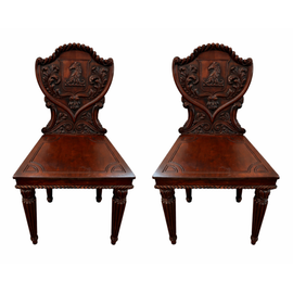 Pair of English William IV carved mahogany hall chairs, c.1830, with heraldic shield backs, horse‑head cresting, acanthus carving, solid seats, and fluted turned legs