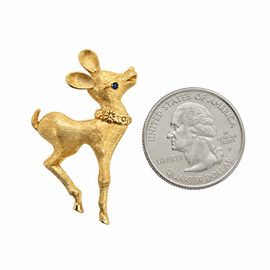 Front view of a vintage 14K yellow gold reindeer pin with a textured Florentine finish and blue sapphire eye ext to a quarter for scale