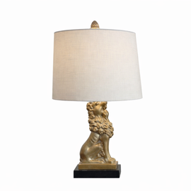 Mid‑century table lamp with a gold patinated seated lion base on a black plinth and a beige drum lampshade with pinecone finial.