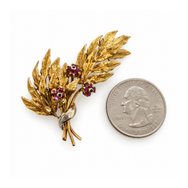 view of vintage 18K yellow gold leaf spray brooch with three ruby and sapphire flowers next to a quarter for scale